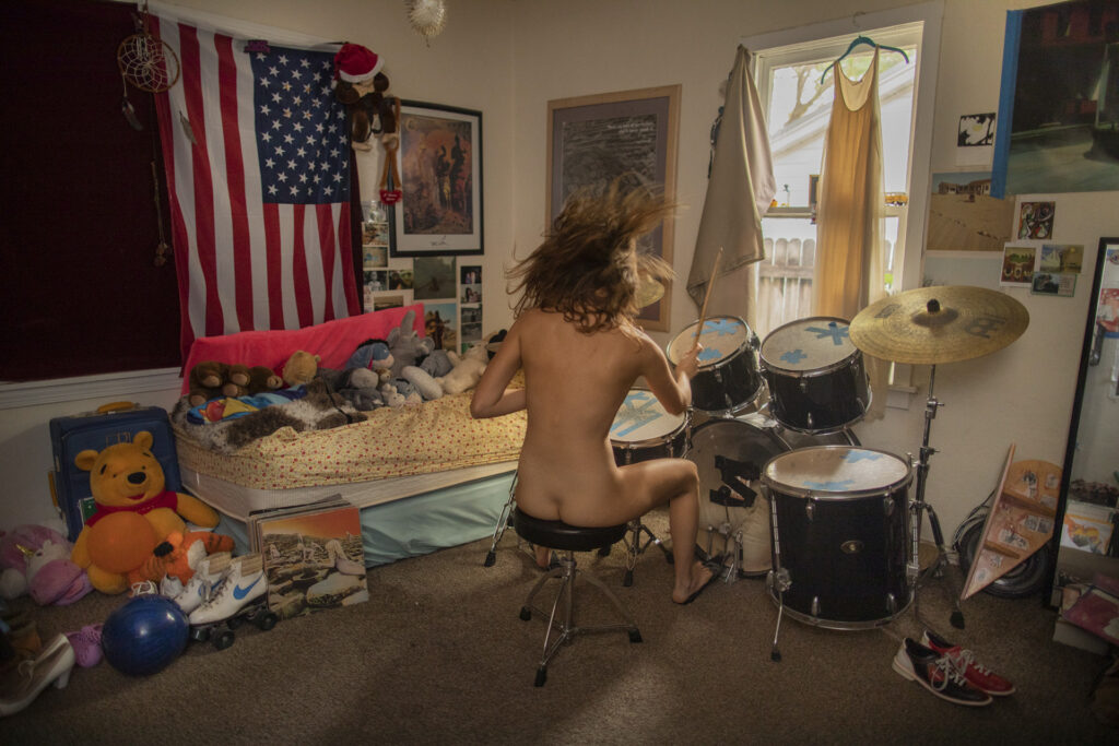 a naked person from behind playing the drums in a room with an american flag