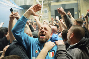 A man with his eyes closed and a Napoli shirt celebrating in the middle of a crowd