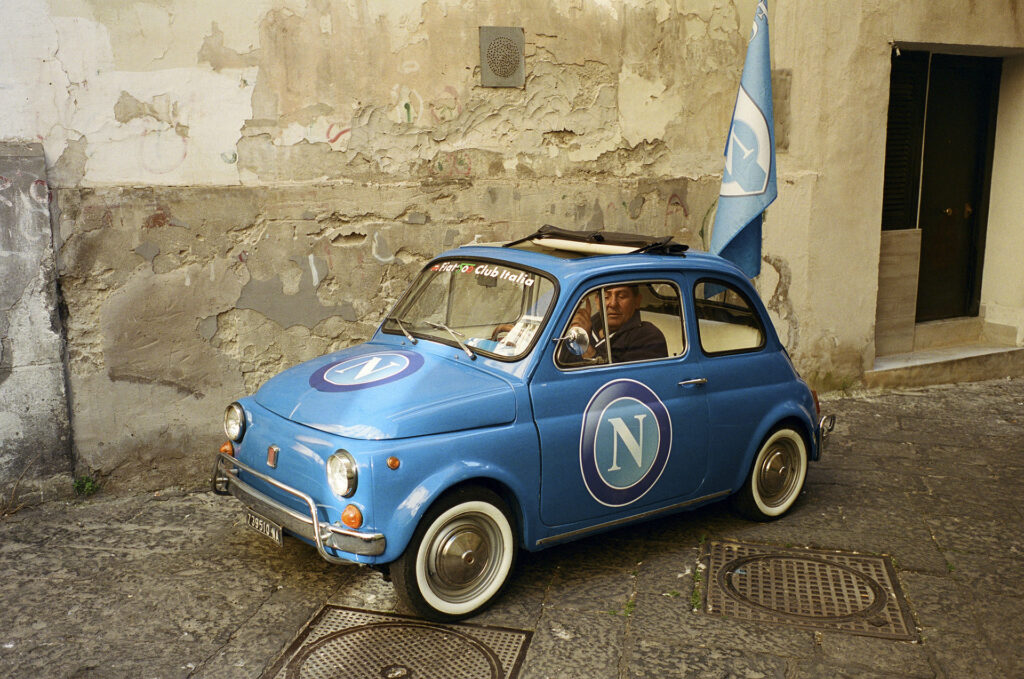 a blue Fiat 500 car with Napoli team logo and flag