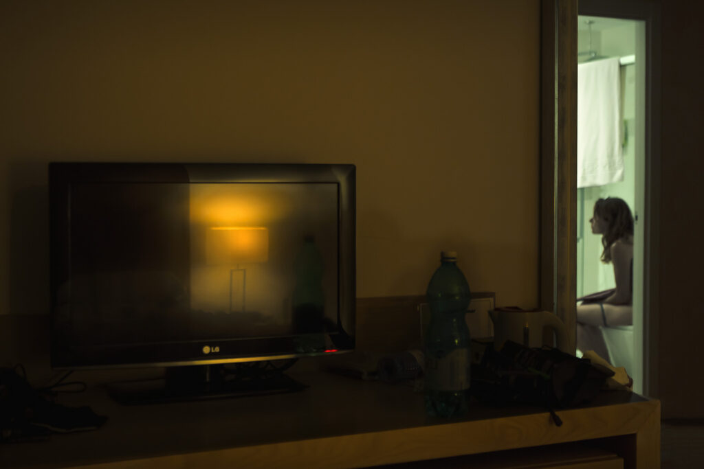 television with a reflected lamp on and behind it a girl sitting on the toilet