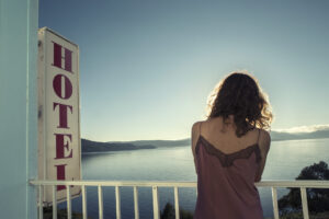 girl on a balcony in front of the sea with a vertical billboard of Hotel in red