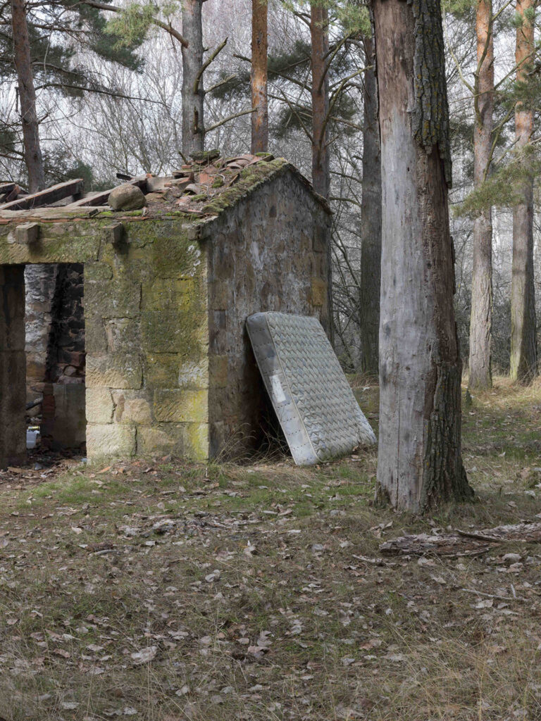 abandoned house in the woods with a mattress leaning against the outside wall