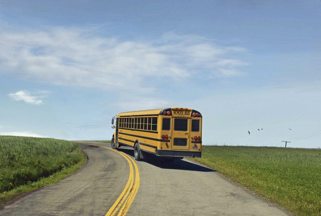 Yellow school bus on a road in the middle of the field, taking a curve