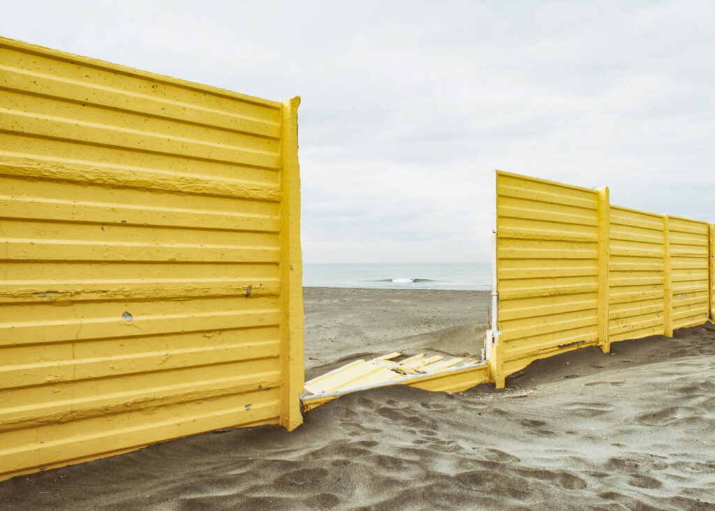 Yellow metal fence on the beach through which you can see a small wave in the sea