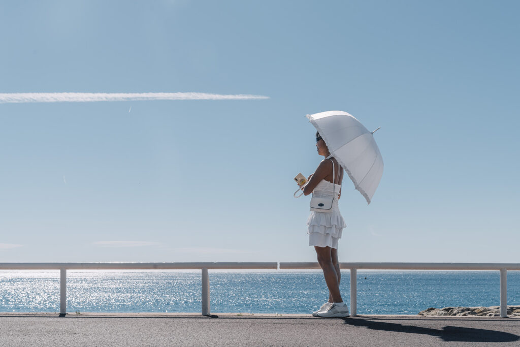 girl with white umbrella on a sunny day on the promenade and in the sky a plane passing